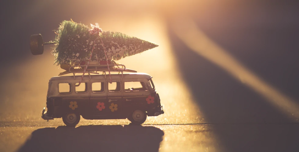 Furgoneta de juguete con un árbol de Navidad en la baca, a contraluz